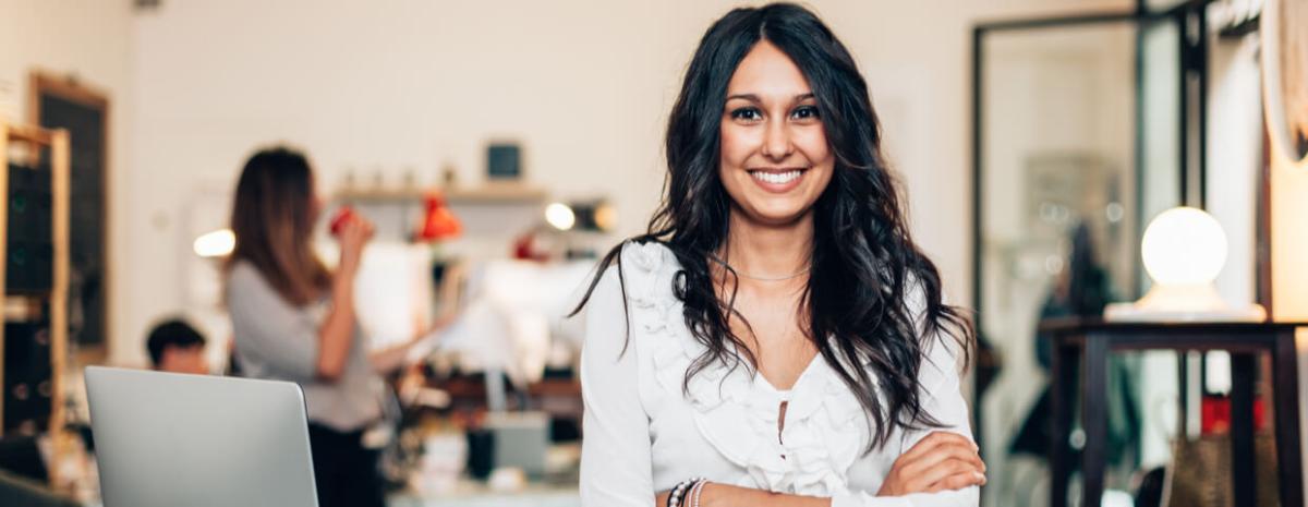 A young woman smiling with hands crossed whille standing in busy office.