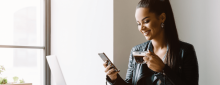 Young woman smiling while holding mobile phone and cup of coffee. Working remotely.