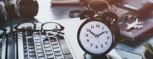 Clock next to laptop, glasses sitting on keyboard